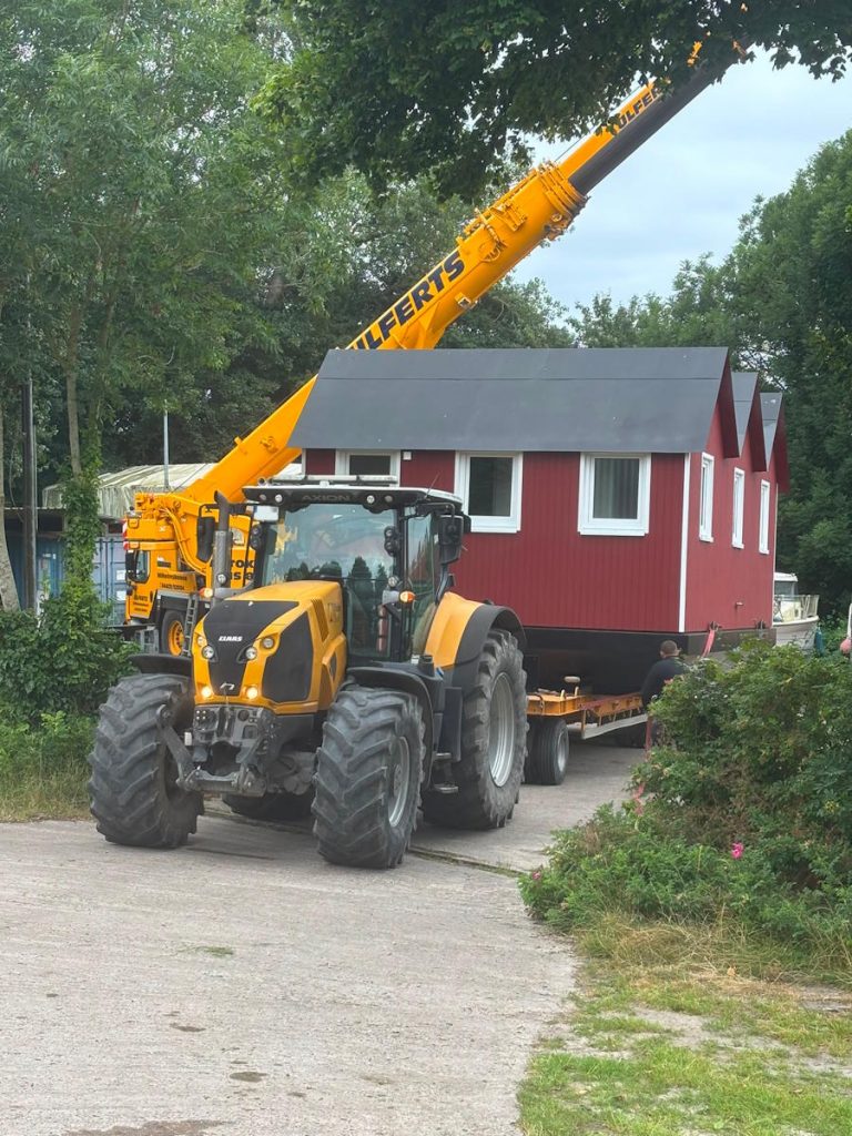 Die Sanitäranlage wird von einem Autokran auf den Tieflader aufgeladen, der an einem Trecker angehängt ist.